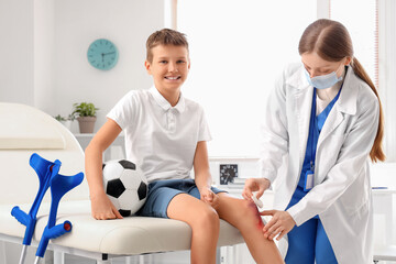 Smiling little boy with wounded knee and soccer ball visiting doctor in clinic