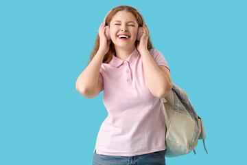 Happy female student with backpack and headphones on blue background