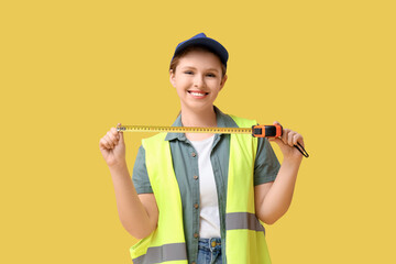Young female carpenter with measuring tape on yellow background. Labor Day celebration
