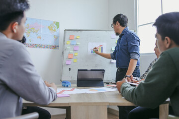Asian Instructor Actively Engages Group Of Young Men In Discussion Pointing To Whiteboard