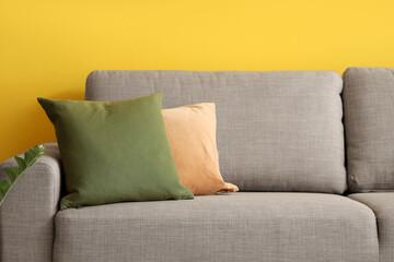 Soft couch with cushions near yellow wall