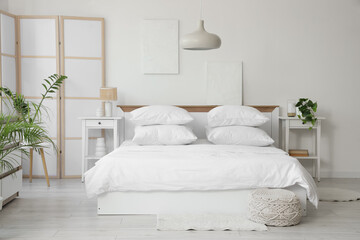 Interior of light room with white linen on bed, folding screen and tables