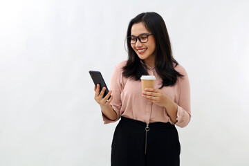 Young Asian woman standing while using mobile phone, smiling celebrating success, enjoying drinking coffee in paper cup, wearing glasses and formal shirt, isolated on white background.