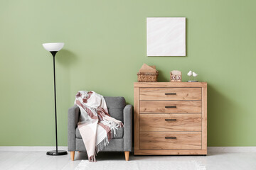 Wooden chest of drawers with cube calendar, books, decor, armchair and lamp near color wall