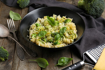 Bowl of delicious fusilli pasta with broccoli and basil leaves on wooden background