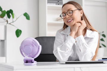 Young businesswoman with mini fan at table in office