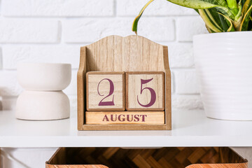 Cube calendar with date 25 AUGUST on shelf near white brick wall, closeup