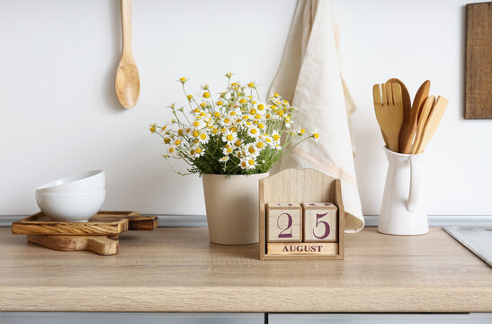 Cube calendar with date 25 AUGUST and chamomiles on counter in kitchen