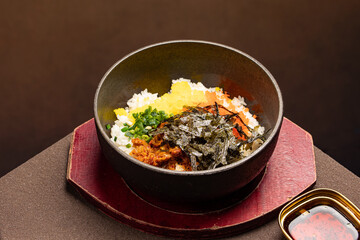 Hot stone pot Korean rice dish (Dolsot Albap) topped with flying fish roe, vegetables, and sesame oil. A sizzling bowl of mixed rice served in traditi
