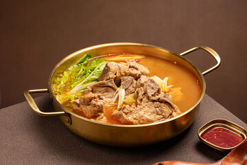 Top view of Korean pork bone stew (Gamjatang) with tender meat, napa cabbage, potatoes, and perilla leaves in a deep red spicy broth. A hearty traditional dish served in Korean cuisine with rich flavo