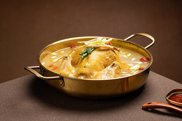 Top view of traditional Korean chicken hot pot (Dakhanmari) with whole chicken, green onions, potatoes, and garlic in a clear savory broth. A healthy and comforting dish served in Korean cuisine.
