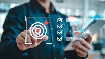 Businessman s hand interacting with a digital interface displaying a dartboard with an arrow hitting the bullseye and a checklist on a tablet
