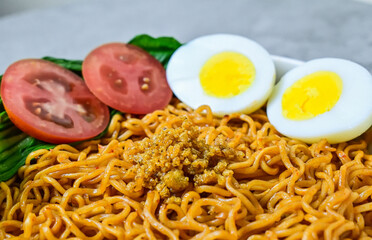extreme close up view of fried instant noodle with sliced of boiled chicken egg, tomato and mustard leaves on the plate. 