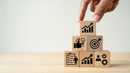 Hand placing wooden block with growth chart icon on stacked blocks representing business success and strategy