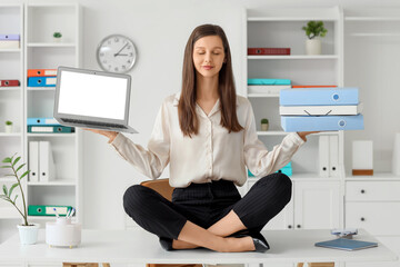 Young businesswoman with blank laptop and folders meditating on table in office