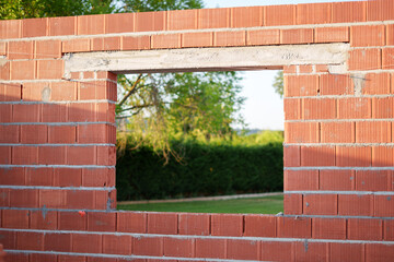 Unfinished brick wall with open window frame offering a peaceful view of the green garden in a...