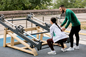 Young woman with personal trainer exercising on sport ground