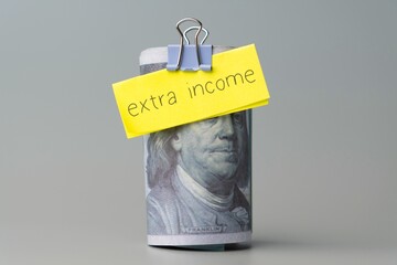 A hundred dollar bill with a note "extra income". Finance concept.