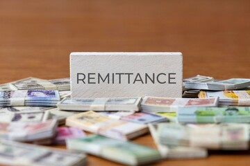 A block with the word "REMITTANCE" surrounded by stacks of various international currencies. Financial concept.