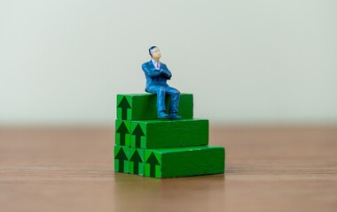 A miniature businessman sit on top of a wooden blocks with upward pointing arrow. Growth, upskill concept.