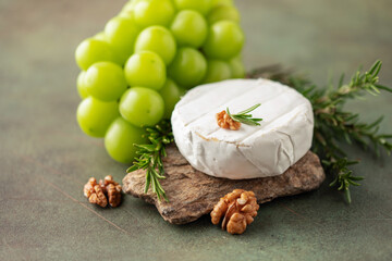 Soft brie or camembert cheese on a stone board, chine muscat grapes, walnut and rosemary branches...