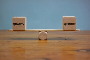 Wooden Blocks Representing Quality and Quantity Balanced on a Wooden Scale