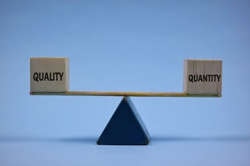 Wooden Blocks Representing Quality and Quantity Balanced on a Wooden Scale