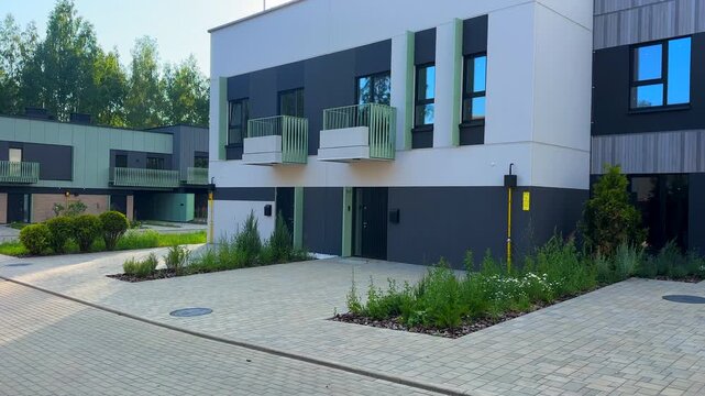Modern townhome design. Modern townhouse with gray white facade building exterior. Modern two-story house with garage. Ornamental thuja shrub in yard. Front yard building exterior of townhouse. 