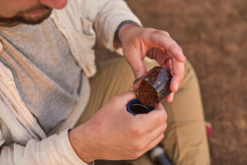 Person pouring ground coffee. Male traveler making coffee for breakfast outdoors early in the...