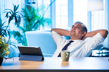 Asian executive leans back on chair at office desk, taking a break from work