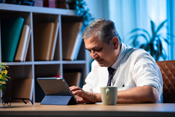 Asian businessman uses tablet computer while sitting in sleek office workspace