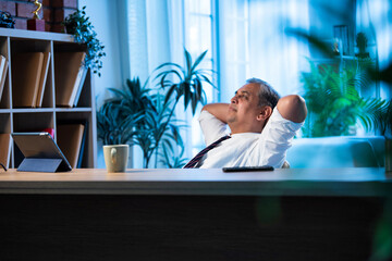 Asian executive leans back on chair at office desk, taking a break from work