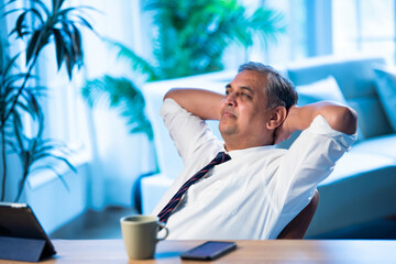 Asian executive leans back on chair at office desk, taking a break from work