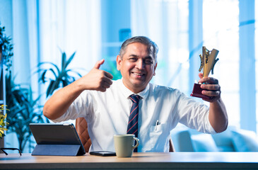 Mid age Indian businessman proudly holding trophy and smiling in stylish office