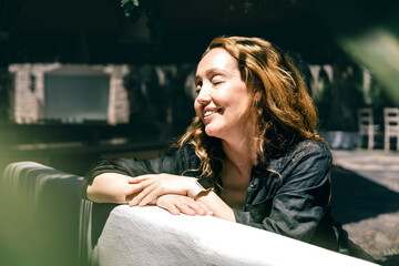 Happy Woman Enjoying Sunlight Outdoors with Closed Eyes and Relaxed Smile in Cozy Garden Cafe