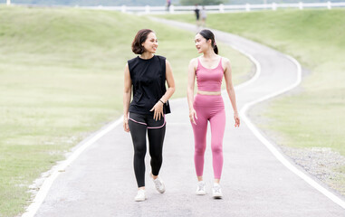 Two young women in workout clothes are walking together in a park.