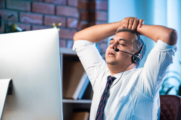 Stressed Indian support agent handling nonstop calls with headset in busy office