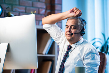 Stressed Indian support agent handling nonstop calls with headset in busy office