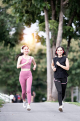 Two Young women wearing headphones in workout clothes are jogging together in a park.