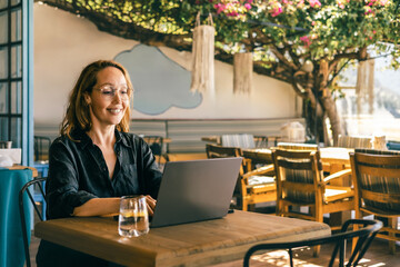 Woman Working on Laptop Outdoors in Cozy Cafe with Natural Light, Relaxed Freelance Lifestyle