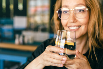 Happy Woman Holding Glass of Water with Lemon, Smiling in Cozy Cafe, Healthy Lifestyle, Relaxation