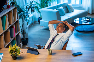 Asian executive leans back on chair at office desk, taking a break from work