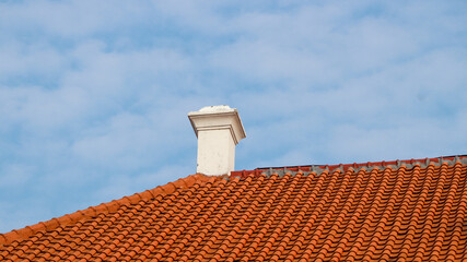 A white colonial-style building with a roof made of red clay tiles under a bright blue sky.