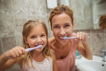 a smiling mother and daughter brushing their teeth in the bathroom at home