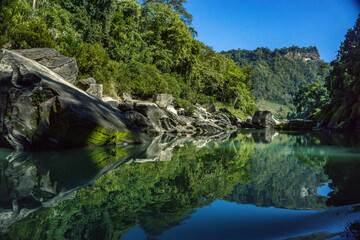 Fototapeta premium Scenic river flowing through a lush, forested landscape reflecting on calm water. Bandarban, Bangladesh is renowned for its stunning natural beauty and adventurous attractions.