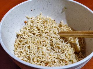 Chewy white instant noodles are held up in a white bowl, highlighting their texture and...