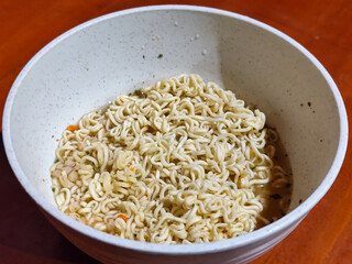 Chewy white instant noodles are held up in a white bowl, highlighting their texture and...