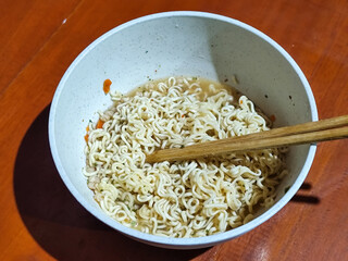Chewy white instant noodles are held up in a white bowl, highlighting their texture and...