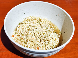 Chewy white instant noodles are held up in a white bowl, highlighting their texture and deliciousness, against the blurry background of the bowl.
