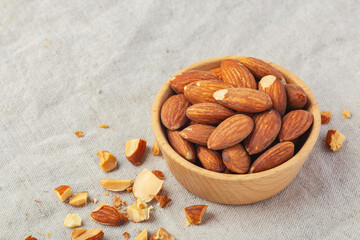 Roasted almonds in wooden bowl on linen table cloth background